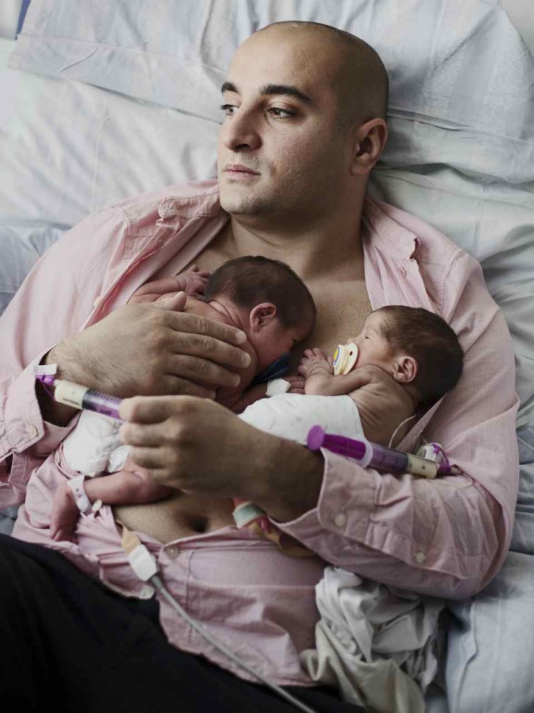 Man lies down with twin infants in his arms.